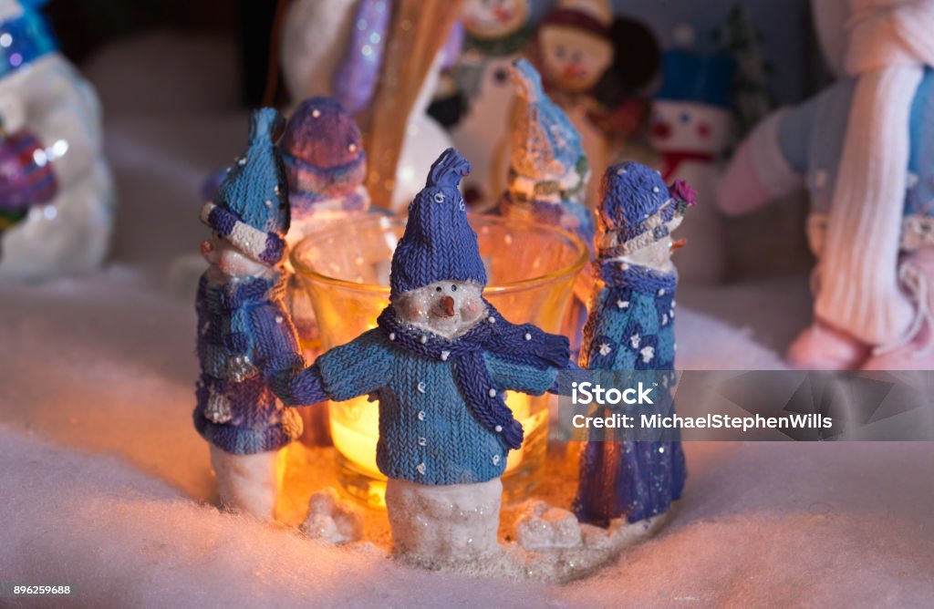 Cozy Christmas Snowmen Five snowman figures dressed in sweater and cap holding hands in a circle.  Each faces away from a central lighted candle in a Christmas tableau. Blue Stock Photo