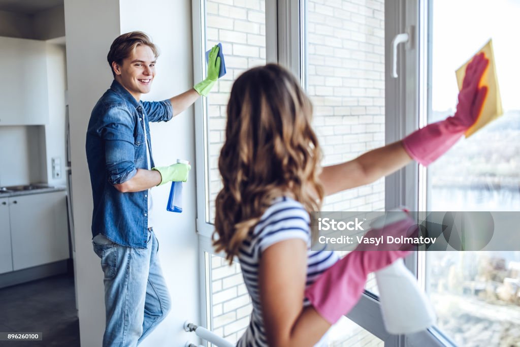 Couple is doing cleaning at home. Young happy couple is washing windows while doing cleaning at home. Cleaning Stock Photo