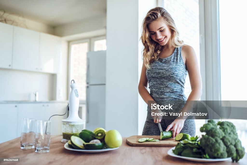 Sporty young woman with healthy food. Sporty young woman is preparing healthy food on light kitchen. Green healthy food concept. Women Stock Photo