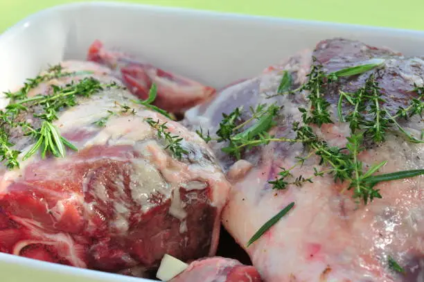 A close up view of fresh raw lamb sprinkled with thyme and ready to cook in a white glass container.