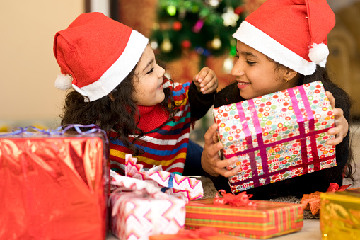 Girl in Santa hat giving Christmas present to her little sister
