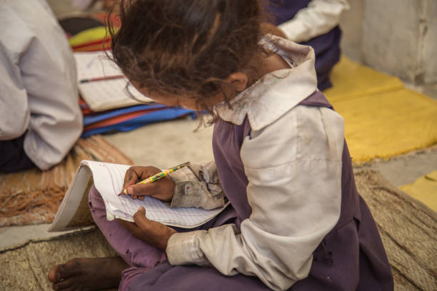Poor Indian village school girl sitting on floor and doing her school assignment. She is shitting on the mat bought from home.