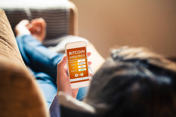 istock Bitcoin - USD converter app in a mobile phone screen while woman holds it lying down on the sofa at home. 896324896