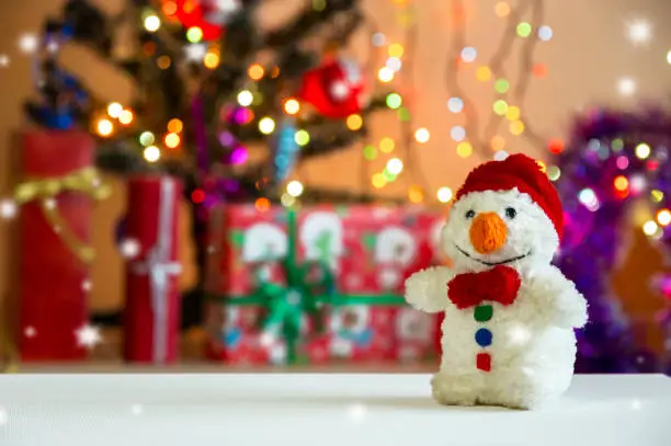 Beautiful Christmas still-life with Christmas decorations and attributes of New Year's holidays. Funny toy snowman in the foreground, against the background of a multicolored glowing garland.