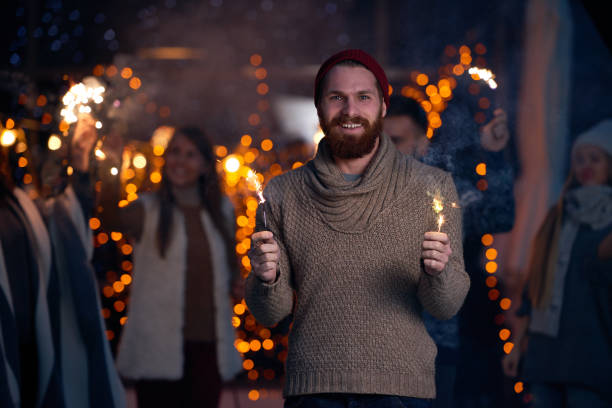 Cheerful excited guy with beard holding burning sparklers celebrating New Year at night outdoors