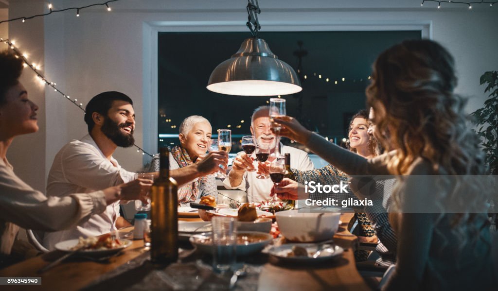 Family having dinner on Christmas eve. Closeup side view of a family having a Christmas eve dinner. They are having some traditional roast, gravy and vegetables and also some vegetarian food. There are three men and four women at the table having casual conversation. Family Stock Photo