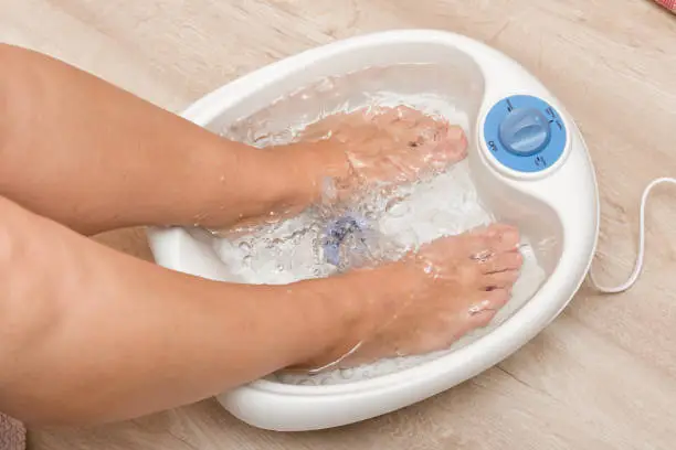 Photo of Female feet in a vibrating foot massager. Electric massage foot bath. Pedicure and foot care