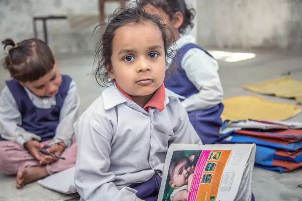 Photo of Rural Indian Pre school Kids sitting on the floor of their classroom.