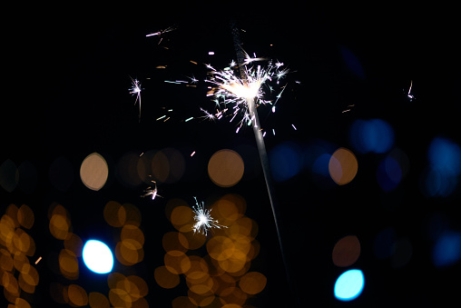 Close-up of festive Christmas sparkler burning against city lights