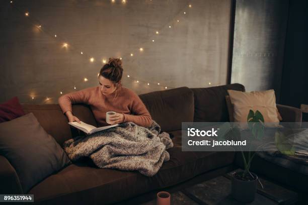 Woman Reading Book In Cozy Living Room Stock Photo - Download Image Now - Blanket, Sofa, Cozy