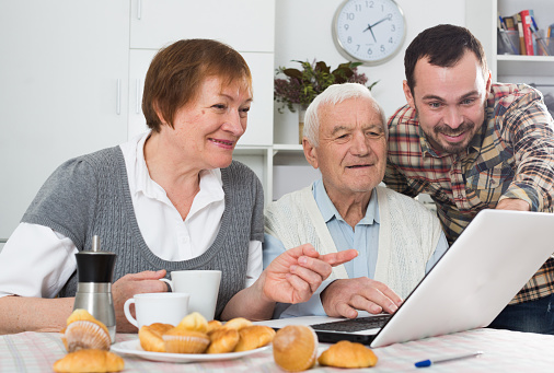 Smiling grandparents and grandson look interesting news on Internet on laptop at home