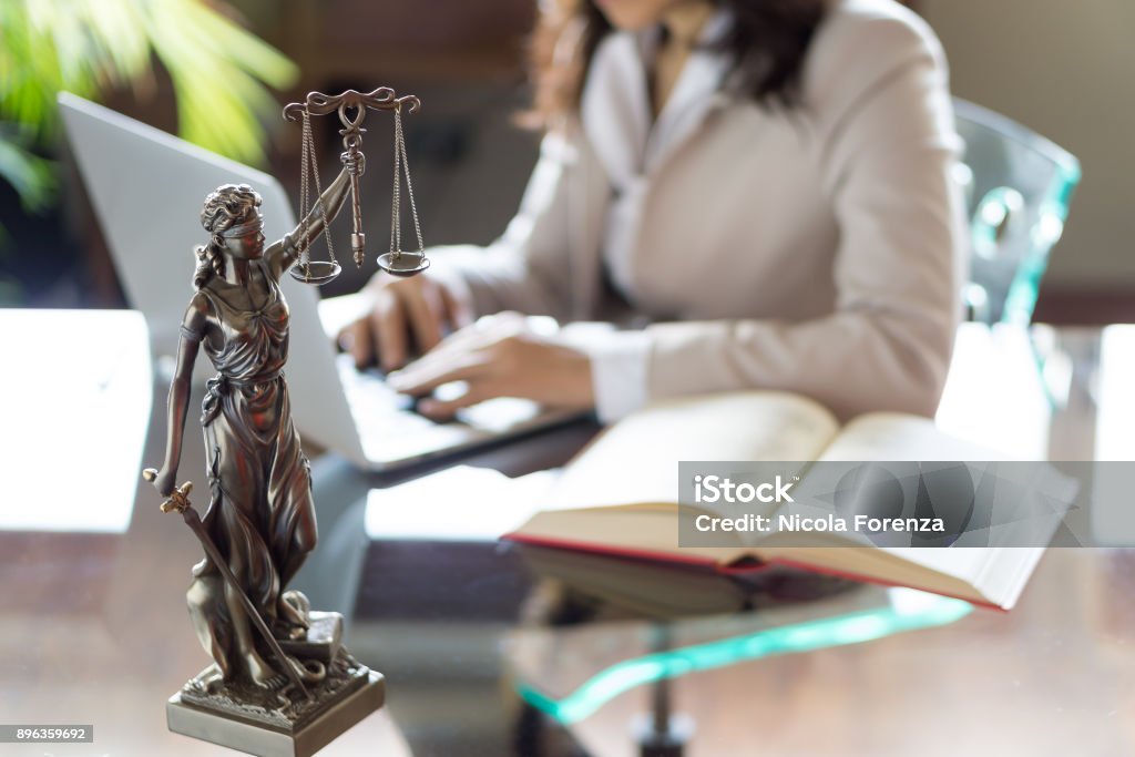 Lawyer office. Statue of Justice with scales and lawyer working on a laptop. Legal law, advice and justice concept Lawyer Stock Photo