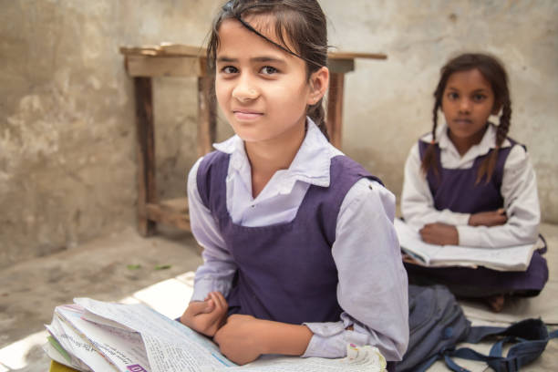 school girl in uniform of indian ethnicity sitting in their village classroom, looking at camera smiling. - emotional stress looking group of people clothing imagens e fotografias de stock