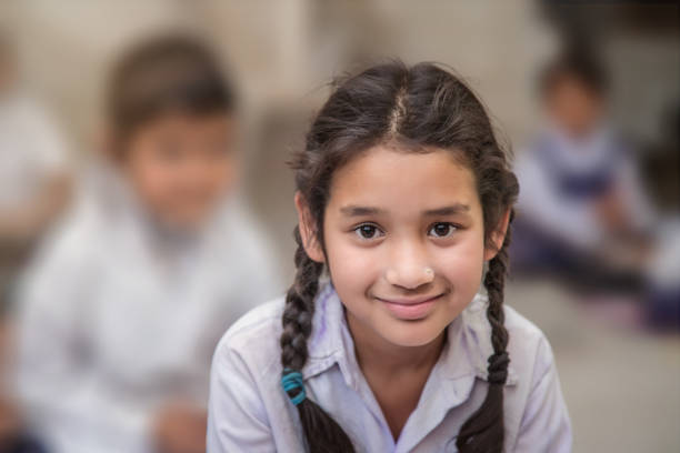 colegiala en uniforme de la etnicidad india sentada en su salón de la aldea, mirando a la cámara sonriendo. - africa child village smiling fotografías e imágenes de stock