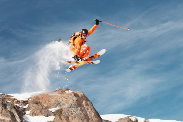 An athlete skier is jumping from high rock high in the mountains