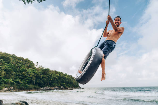 reifenschaukel am tropischen strand - men swing rope swing tire stock-fotos und bilder