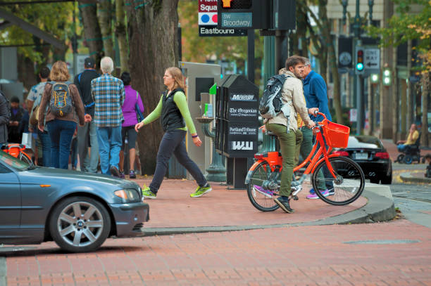 Portland, Oregon,USA - October 8, 2016:  A man on a orange Portland rental bicycle is waiting to cross a downtown crossroads where cars, pedestrians and bicyclist travel across.