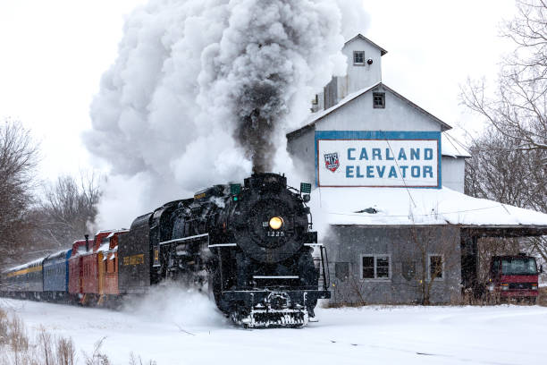 CARLAND, MICHIGAN,USA-DECEMBER 09: Steam engine Pere Marquette 1225 speeds by an abandoned grain elevator on December 9, 2017. This steam engine is known as the North Pole Express and travels between the towns of Owosso and Ashley stock photo