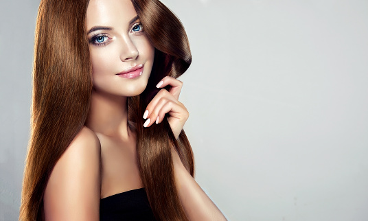 Young, brown haired woman  with voluminous hair.Beautiful model with long, dense, straight hairstyle and vivid makeup, is touching own hair with tenderness. Symbol of attentiveness to hair and good care of it. Perfect hair  and sexy look.Incredibly dense, wavy,and shiny hair.