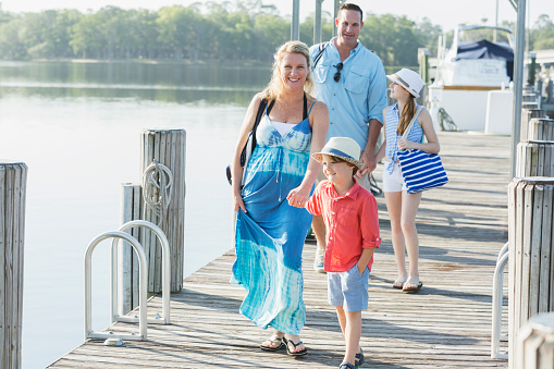 a family with two children, 5 and 11 years old, walking down a wooden pier after a day on a boat. They are smiling at the camera.