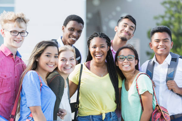 Multi-ethnic group of teenagers at school, outdoors A group of eight multi-ethnic teenagers, 17 and 18 years old, carrying book bags, standing together outside a school building. They are high school seniors or university freshmen. boy and girl looking at camera stock pictures, royalty-free photos & images