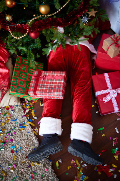 Drunken Santa lying under Christmas tree among gifts