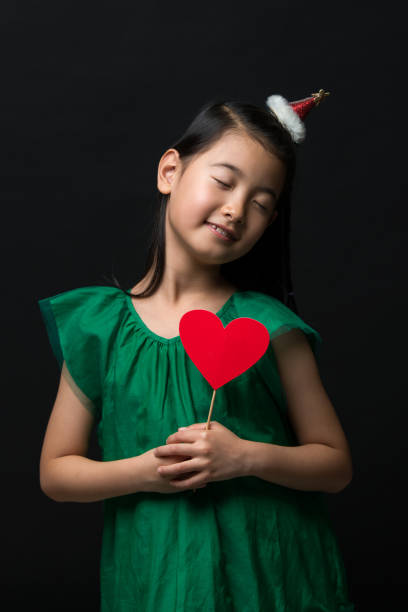 Linda Niña Asiática Vestida Con Un Vestido Verde Con Un Ornamento De La Navidad Y Un Palo De Corazón Sobre Un Fondo Negro Ojos Cerrados Foto de stock y más banco de imágenes de Alegre - iStock Linda Niña Asiática Vestida Con Un Vestido Verde Con Un Ornamento De La Navidad Y Un Palo De Corazón Sobre Un Fondo Negro Ojos Cerrados Foto de stock y más banco de imágenes de Alegre - iStock