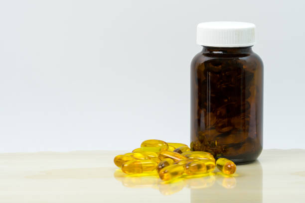 Yellow fish oil capsule pills with amber glass bottle with blank label on the table with copy space for text. Vitamins and supplements for heart care and joint care. Source of omega 3, EPA and DHA. aceite de pescado amarillo píldoras cápsulas con botella de vidrio ambar con etiqueta en blanco sobre la mesa con espacio de copia de texto. vitaminas y suplementos para el cuidado del corazón y atención conjunta. fuente de omega 3, epa y dha.