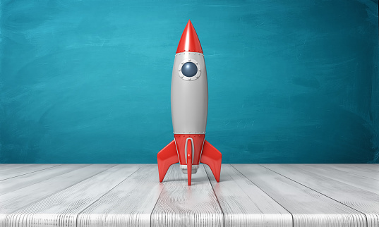 3d rendering of a red and silver realistic model of a retro rocket stands on a wooden desk on a blue background. Science fair. Goals and dreams. Fly in space.