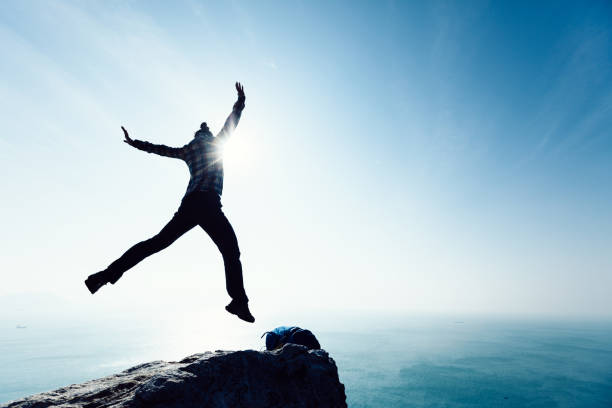 istock free female hiker jumping on sunrise seaside cliff edge 896643448