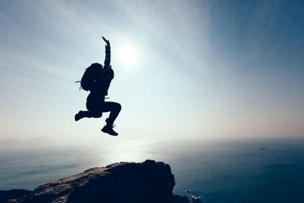 istock free female hiker jumping on sunrise seaside cliff edge 896643648