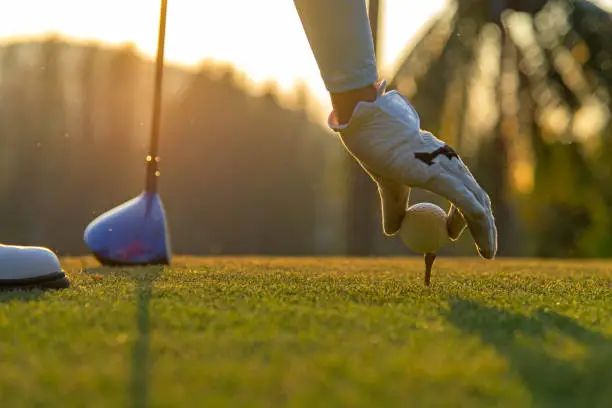 Photo of Hand asian woman putting golf ball on tee with club in golf course on evening and sunset time a for healthy sport.  Lifestyle Concept