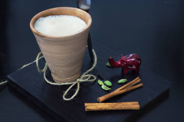 regionalnych środowisk żywnościowych. indyjski masala chai karak herbaty z przyprawami i mlekiem, w szkle glinianym. czarne drewniane tło. selektywna ostrość - cardamom indian culture food spice zdjęcia i obrazy z banku zdjęć