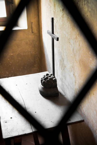istock Enclosure cell seen through an iron grating with wooden crucifix on a table 896683208