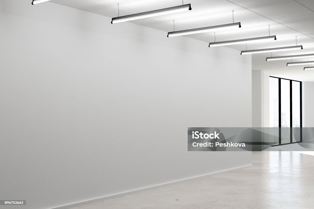 Concrete interior with empty wall Side view of modern office interior with empty concrete wall, lamps and city view. Mock up, 3D Rendering Office Stock Photo