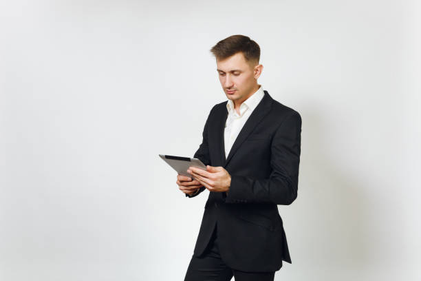 istock Young successful handsome rich business man in black suit working on modern tablet isolated on white background for advertising. Concept of money, achievement, career and wealth in 25-30 years. 896774970