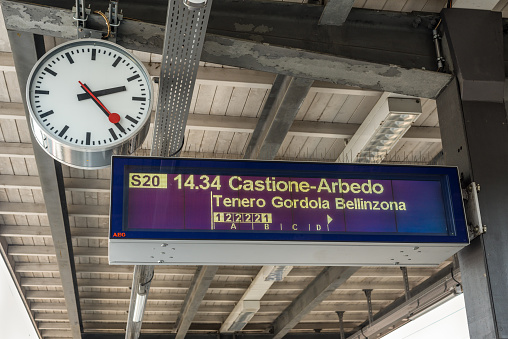 Locarno, Switzerland - May 28, 2016: Electronic departures board and clock over a platform of the Locarno railway station indicating the departure time for a Swiss Federal Railways train to the station of Castione-Arbedo.