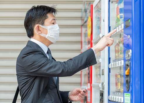 A Japanese man choosing from a variety of soda and coffee drinks at a vending machine on the street in Tokyo.