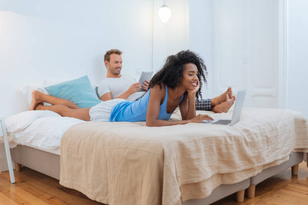 istock Happy young couple relaxed at home lying down in bed on the tablet and computer 