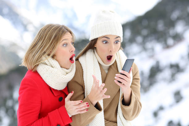 Amazed friends with a smart phone in winter Two amazed friends with a smart phone in winter holidays in a snowy mountain christmas excitement stock pictures, royalty-free photos & images