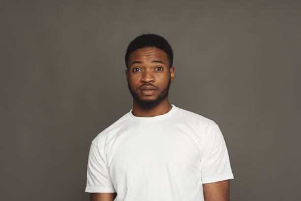 Surprised facial expressions, black man Black man expressing surprise, standing on grey background, studio shot sheepish look stock pictures, royalty-free photos & images