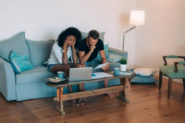 istock Young interracial couple in the couch stressed with financial problems doing calculations with paper work