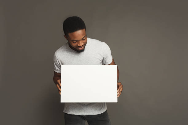 Picture of young african-american man holding white blank board Picture of young smiling african-american man holding white blank board on grey background, copy space holding hands photos stock pictures, royalty-free photos & images