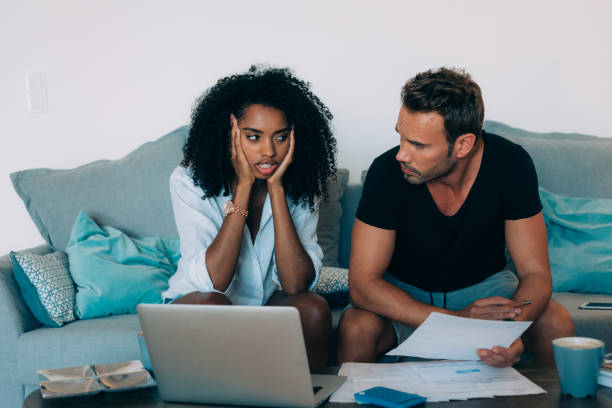 istock Young interracial couple in the couch stressed with financial problems doing calculations with paper work
