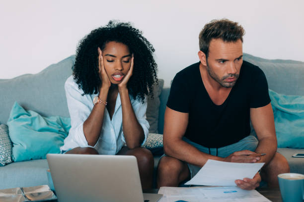 istock Young interracial couple in the couch stressed with financial problems doing calculations with paper work
