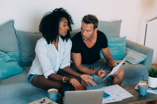 istock Young interracial couple in the couch stressed with financial problems doing calculations with paper work