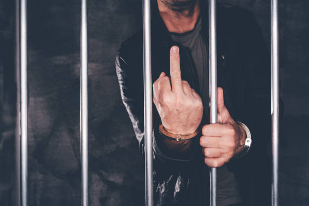 istock Handcuffed man behind prison bars giving middle finger 896891090