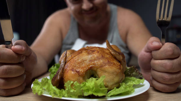 istock Fat man preparing to eat greasy fried chicken, holding knife and fork, close-up 896909496