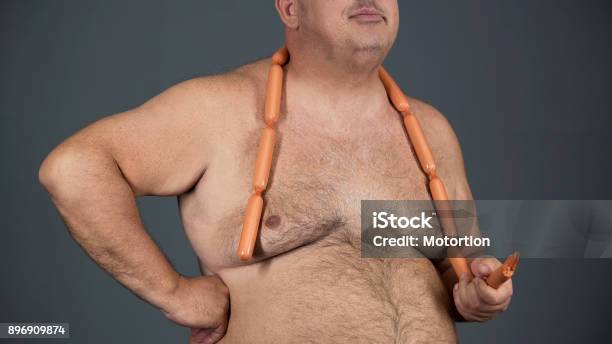 Chubby Man Eating Sausages With Appetite Food Addiction Risk Of Diabetes Stock Photo - Download Image Now