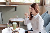 カフェでケーキを食べてフォークで魅力的な若いアジア女性の肖像画。